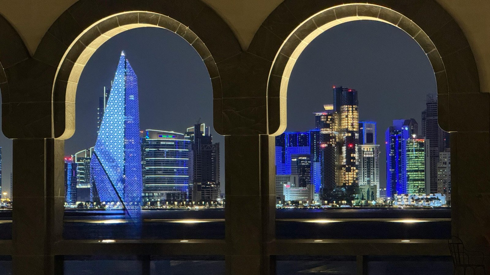 Stunning night view of Doha skyline seen through decorative archways, reflecting vibrant city lights. kwesttzadventures Doha